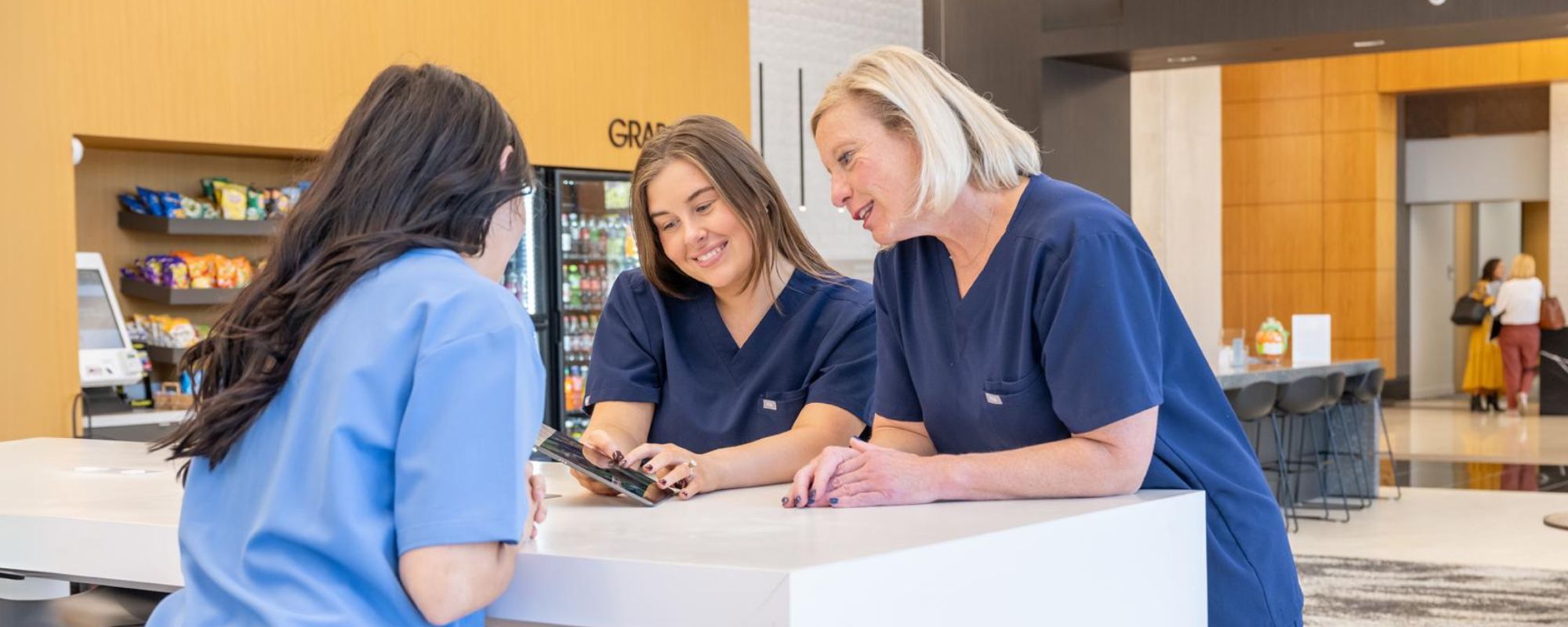 3 healthcare workers at a table all smiling and looking at a phone