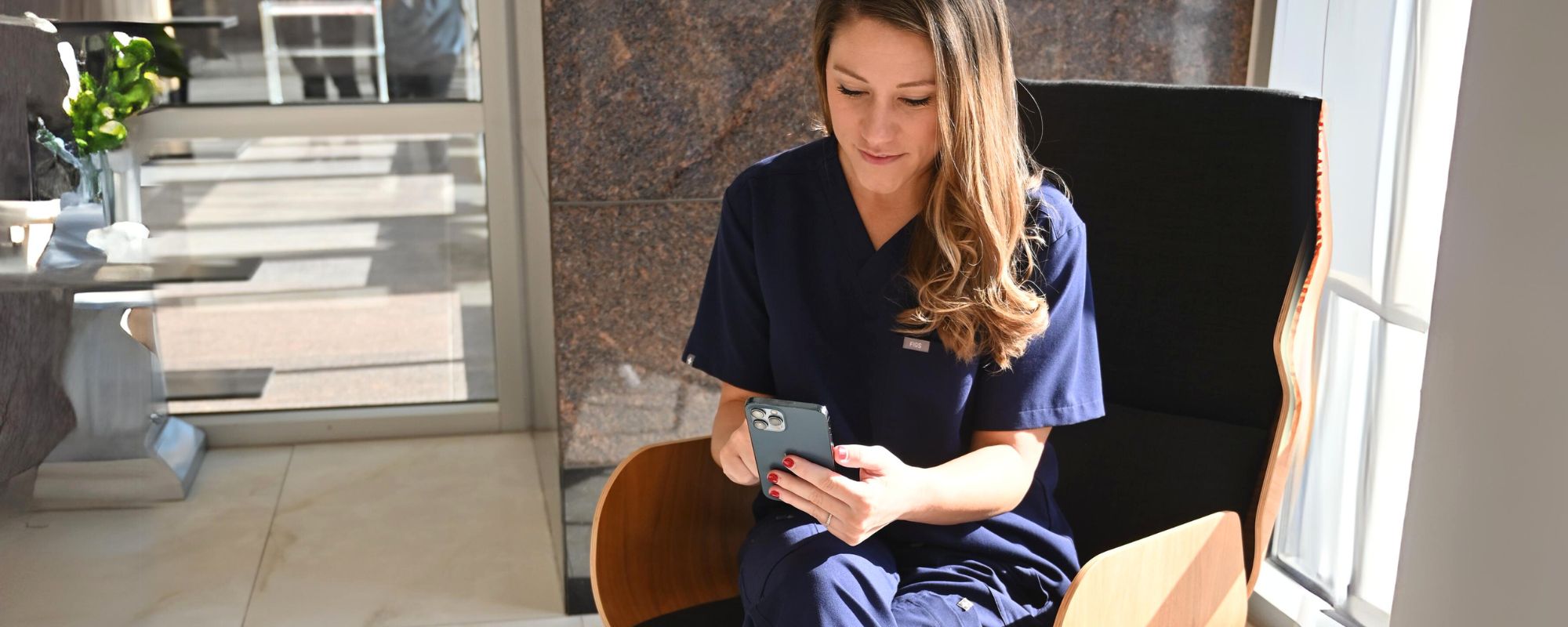 female healthcare worker sitting in lobby while using her phone