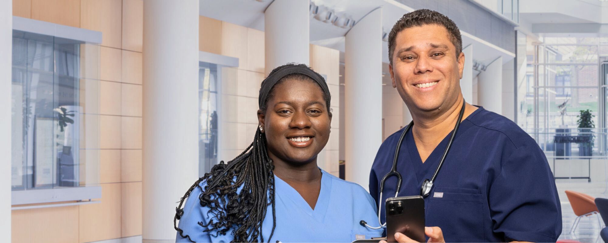 two healthcare workers in a hospital holding a phone and smiling at the camera