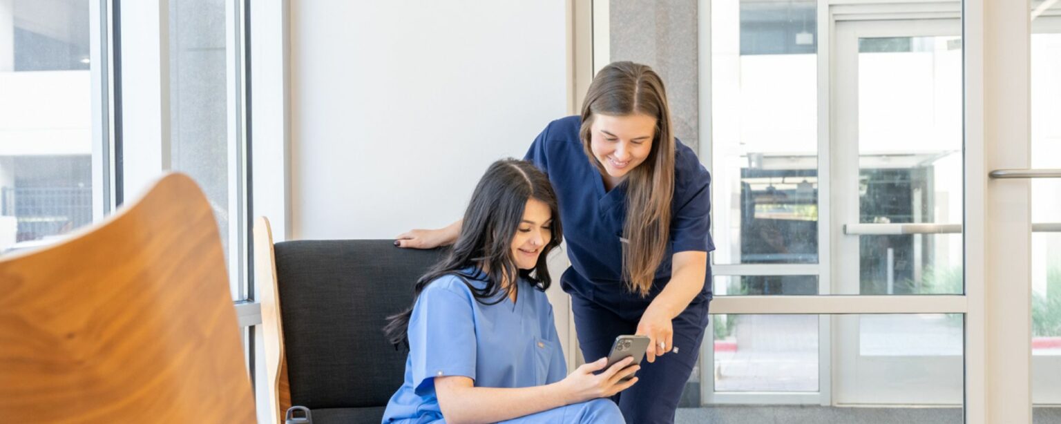 2 women healthcare workers looking at phone smiling