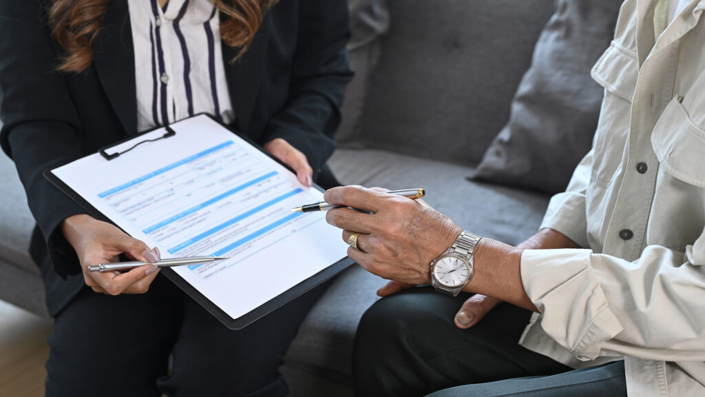 Cropped shot of elderly man sitting in insurance agency office and signing on health insurance.