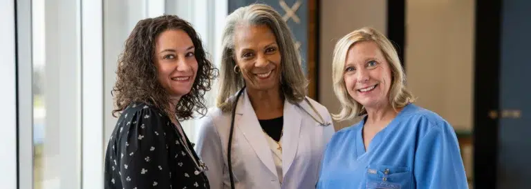 Two female doctors and a female nurse smiling at camera.