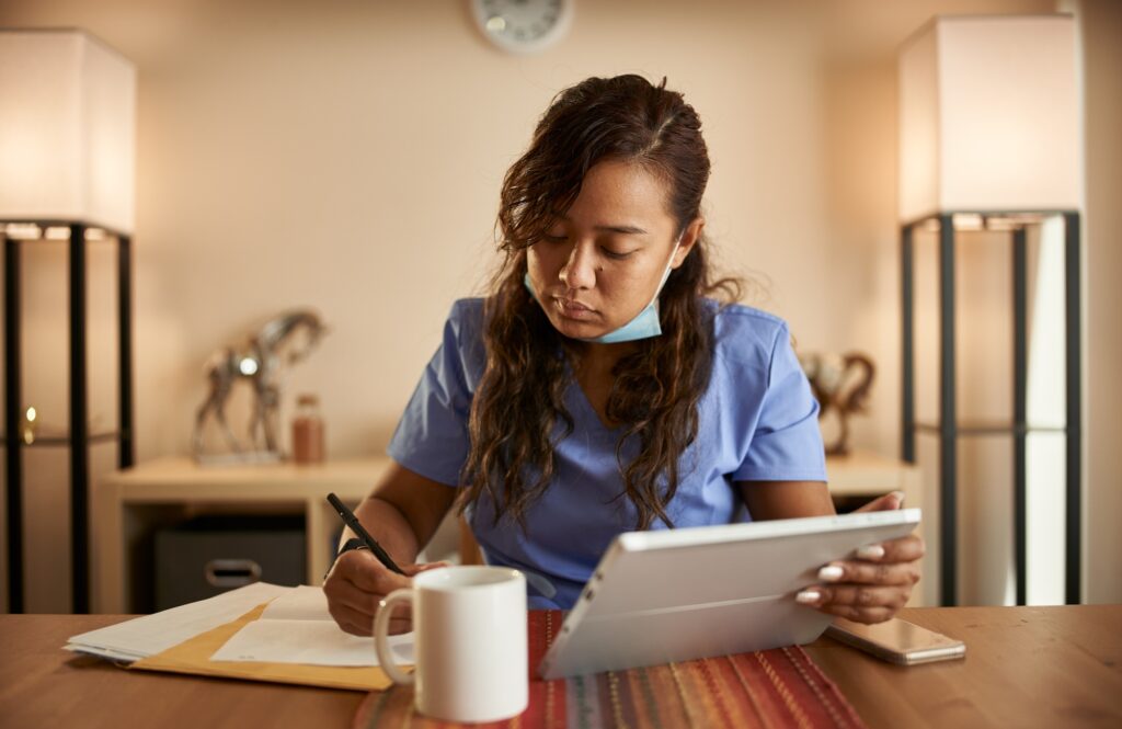 filipina nurse working from home doing paperwork and using tablet