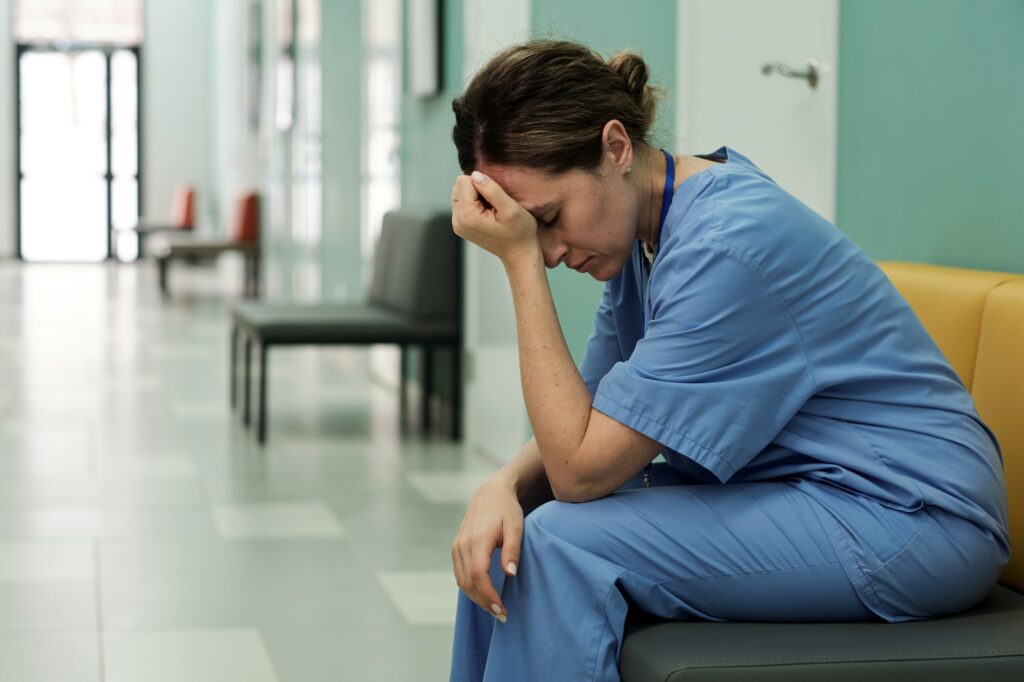 Young tired or stressed female doctor sitting in hospital corridor