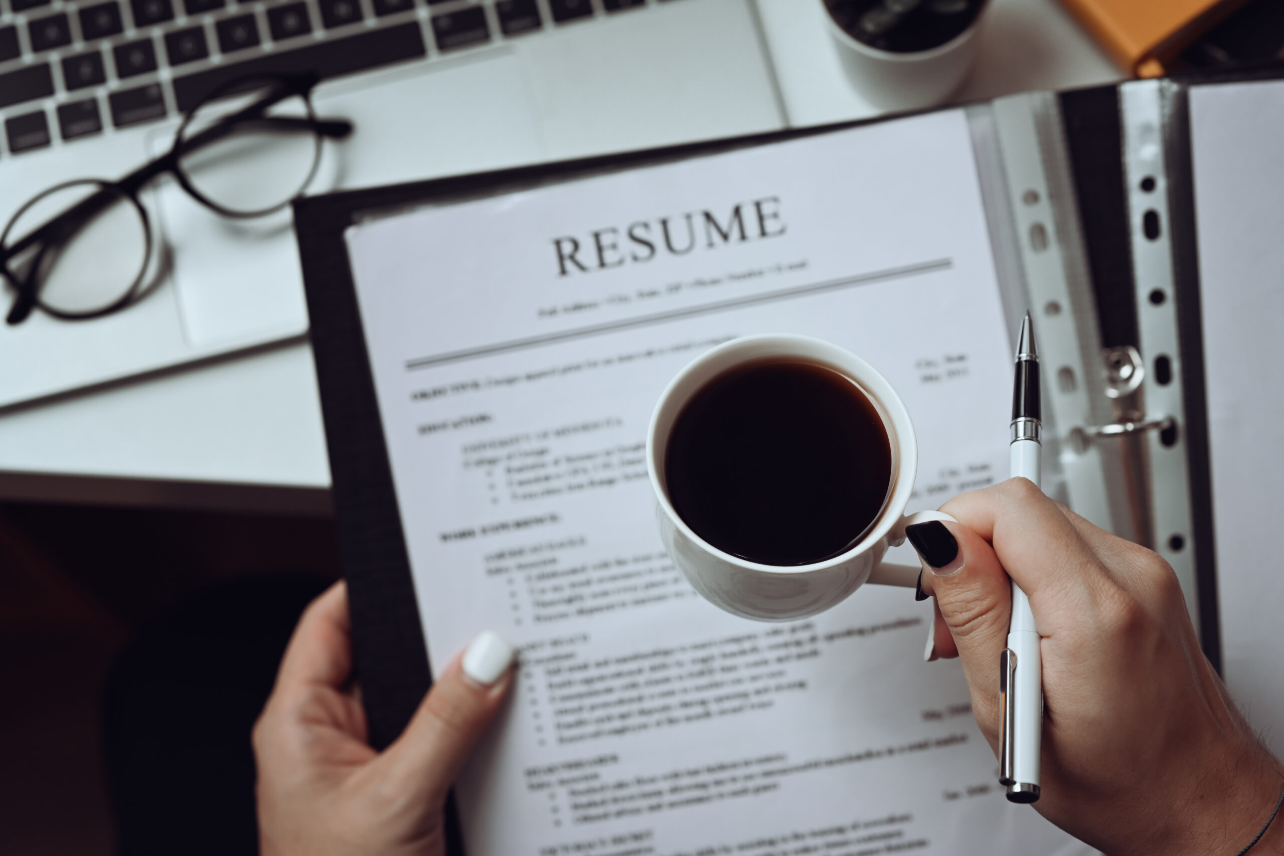 Picture of a woman holding coffee while looking over resume at desk.